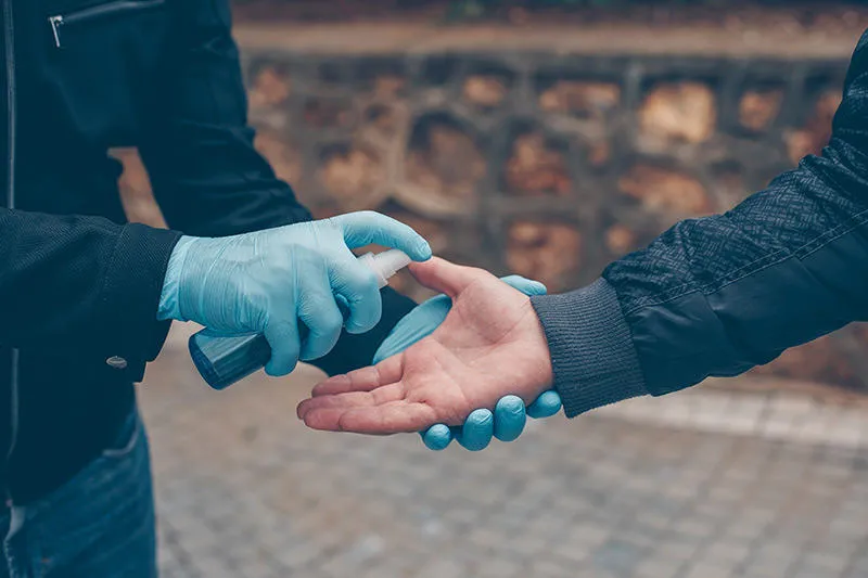 A person wearing blue gloves spraying hand sanitiser